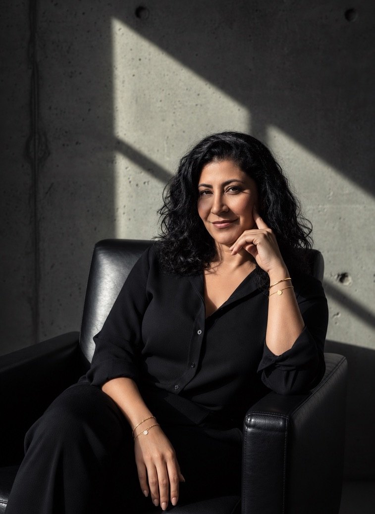 Nadine Kiwan sitzt in einem schwarzen Ledersessel vor einer Betonwand mit Fensterlicht und blickt lächelnd in die Kamera